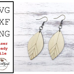May include: A pair of wooden leaf-shaped earrings with etched linear details. The earrings are light-colored with dark metal hooks. The image also includes text: SVG, DXF, PNG, Laser Ready File, and the Blessed Soul Creations logo.