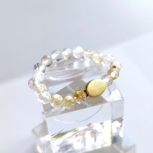 May include: A gold ring with a clear and yellow crystal bead design. The ring has a gold clasp.