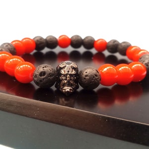 May include: A bracelet made with black lava rock and red beads, featuring a skull charm.