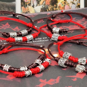 May include: A set of red and brown string bracelets with silver charm beads. The bracelets have a variety of designs, including a Buddha head, a heart, and a floral pattern.