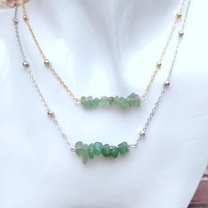 May include: A silver chain necklace with a gold chain necklace layered on top. Both necklaces feature a row of green gemstone chips.