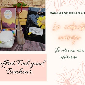 Peut inclure: Un coffret cadeau comprenant un bracelet arc-en-ciel, un petit support conique, un petit sachet de cristaux de calcite orange et une carte qui dit "Le Petit Livre du Bonheur" avec une scène de montagne. La boîte est étiquetée "Coffret Feel good Bonheur". Le texte "La calcite orange" et "Je retrouve mon optimisme." est écrit en lettres néon roses sur un fond blanc avec un motif floral.