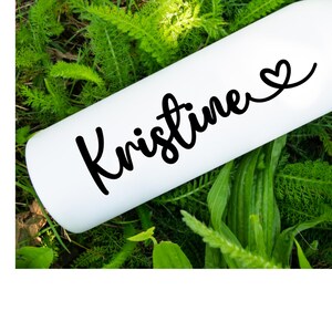 Puede incluir: Botella de agua blanca con el nombre "Kristine" escrito en cursiva negra y un pequeño símbolo de corazón.