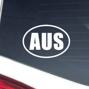May include: White oval sticker with the letters "AUS" in bold, white font. The sticker is on the rear window of a white car. The car's taillight is visible.