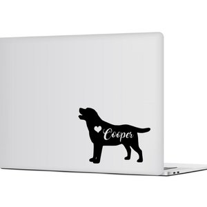 Op de afbeelding: Zwart Labrador Retriever silhouet met een hart en de naam "Cooper" in witte letters op een witte laptop. De hond wordt afgebeeld met zijn mond open, en het ontwerp is een sticker of decal.