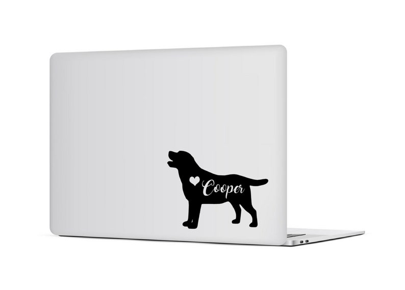 Op de afbeelding: Zwart Labrador Retriever silhouet met een hart en de naam "Cooper" in witte letters op een witte laptop. De hond wordt afgebeeld met zijn mond open, en het ontwerp is een sticker of decal.
