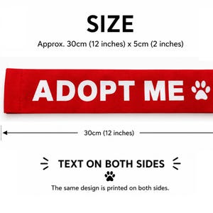 May include: A rectangular red fabric strap featuring the white text ADOPT ME and a white paw print icon. The strap measures 12 inches by 2 inches. The same design is printed on both sides of the fabric, providing clear visibility for pet identification.