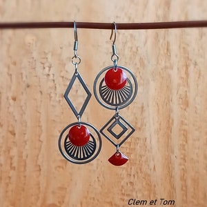 Puede incluir: Un par de pendientes de plata con formas geométricas rojas. Los pendientes tienen un círculo, un diamante y una media luna. Los pendientes cuelgan de un gancho de plata.