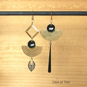 Puede incluir: Un par de pendientes de oro con detalles negros. Un pendiente presenta una forma geométrica de diamante, una cuenta negra, un diseño de medio círculo y un dije de hoja. El otro pendiente presenta un diseño de medio círculo, una cuenta negra y una larga caída negra.