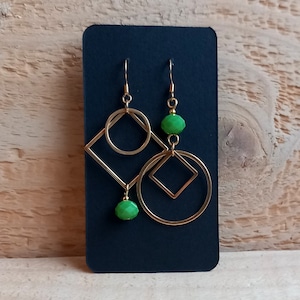 Op de afbeelding: Een paar gouden geometrische oorbellen met groene glazen kralen. De oorbellen hebben een vierkant met een cirkel erin en een hangende groene kraal.