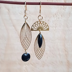 Puede incluir: Pendientes de oro con detalles negros. Un pendiente presenta un diseño de sol geométrico y el otro un diseño de hoja. Ambos pendientes tienen un colgante de cuentas negras.