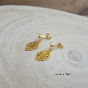 Peut inclure: Boucles d'oreilles pendantes en forme de feuille dorée avec un design délicat et complexe. Les boucles d'oreilles sont composées de deux feuilles superposées avec une petite boule dorée au sommet.
