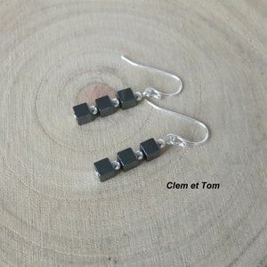 Peut inclure: Une paire de boucles d'oreilles en argent avec quatre perles carrées noires sur chaque boucle d'oreille. Les boucles d'oreilles ont une fermeture à crochet.