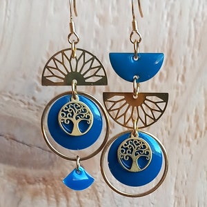 Può includere: Orecchini dorati e blu con un design ad albero della vita. Gli orecchini presentano un cerchio con un albero della vita all'interno, un semicerchio con un design a raggiera e un semicerchio con un design blu pieno.