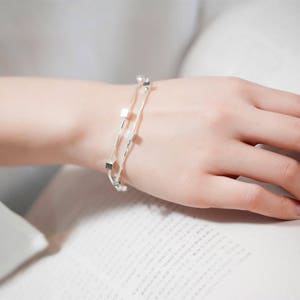 Peut inclure: Un bracelet en argent avec un design à double chaîne et de petits charmes carrés.
