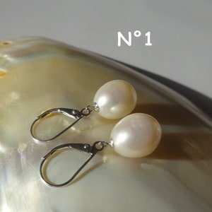 Peut inclure: Une paire de boucles d'oreilles pendantes en argent avec des perles blanches. Les boucles d'oreilles sont présentées sur une coquille de nacre. Le texte "N°1" est visible sur l'image.