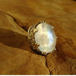 Pode incluir: Um anel de prata com uma grande pedra de lua ovalada engastada em um design de coroa.