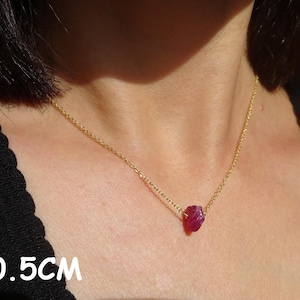 May include: A gold chain necklace with a raw ruby pendant. The necklace is 40.5cm long. The ruby is a deep red colour and is displayed against a skin tone background.