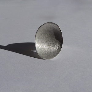 May include: A silver ring with a smooth, rounded, and slightly curved top. The ring is made of metal and has a brushed finish.