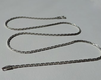 May include: A silver chain necklace with a box chain design. The chain is about 20 inches long and has a lobster clasp closure.