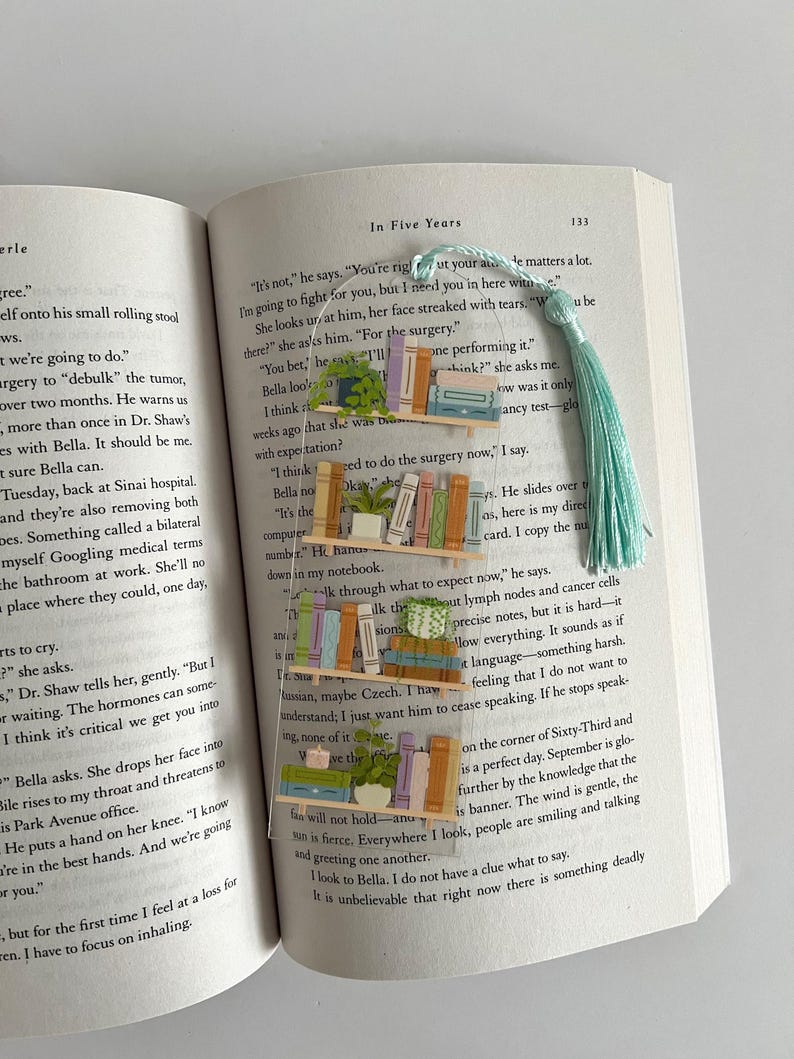 Pu&ograve; includere: Un primo piano di un libro aperto con un segnalibro. Il segnalibro &egrave; un fiocco blu chiaro con una pila di libri colorati e una piccola pianta in vaso. Le pagine del libro sono piene di testo e il segnalibro copre parzialmente il testo. Il testo sulla pagina recita: "Non &egrave;", dice. "Hai ragione per quanto riguarda la tua et&agrave;. Conta molto. Combatter&ograve; per te, ma ho bisogno di te qui con me."