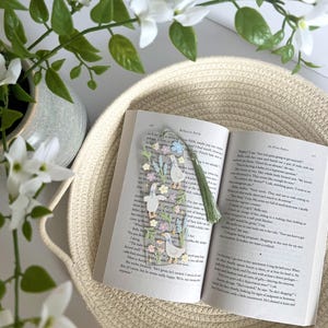 May include: A close-up of a book with a bookmark featuring a floral design and a group of ducks. The bookmark has a green tassel. The book is open to a page with the text "In Five Years" by Rebecca Serle.