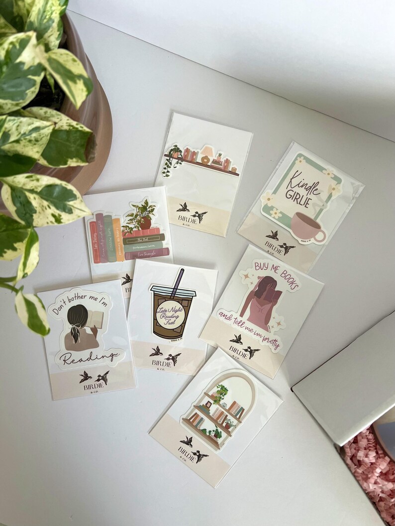 May include: A collection of stickers with various designs, including a coffee cup, a bookshelf, and the text "Kindle Girlie." The stickers feature illustrations and text related to reading and books. The brand name "Birdie & Co" is visible on the stickers.