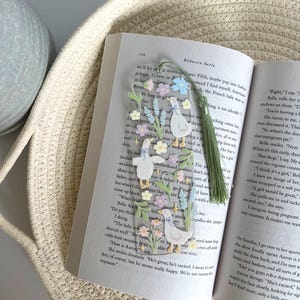 May include: A clear bookmark with a floral design and three white ducks. The bookmark has a green tassel and the text "Right" and "Bella rolls her eyes" is visible.