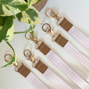 May include: Several pink and white gingham lanyards with gold-tone metal clasps and brown leather details. Each lanyard has a swivel clasp and a small leather tag with the initials "BC" embossed.