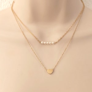 Op de afbeelding: Een gouden gelaagde ketting met een klein hartje en een rij van vijf witte parels.