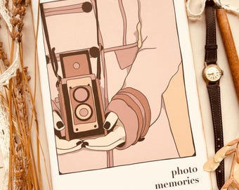 May include: A vintage-style camera with a brown leather strap is held in the hands of a person wearing a pink coat. The image is in a white frame with the text "photo memories" at the bottom.