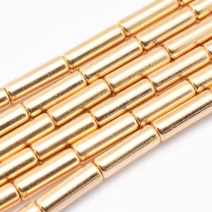 Peut inclure: Perles en métal ton or de forme cylindrique. Les perles sont disposées en rangées, créant un motif répétitif.