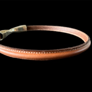 Peut inclure: Un bracelet en cuir marron avec une fermeture en argent. Le bracelet est orné d'un motif cousu.