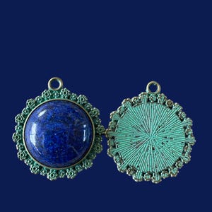 Op de afbeelding: Een paar ronde, sierlijke metalen hangers, een met een blauwe lapis lazuli-steen en de andere met een groen metalen ontwerp.