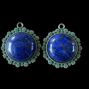 Op de afbeelding: Twee ronde blauwe lapis lazuli edelsteen hangers met een groen filigraan metalen ontwerp.