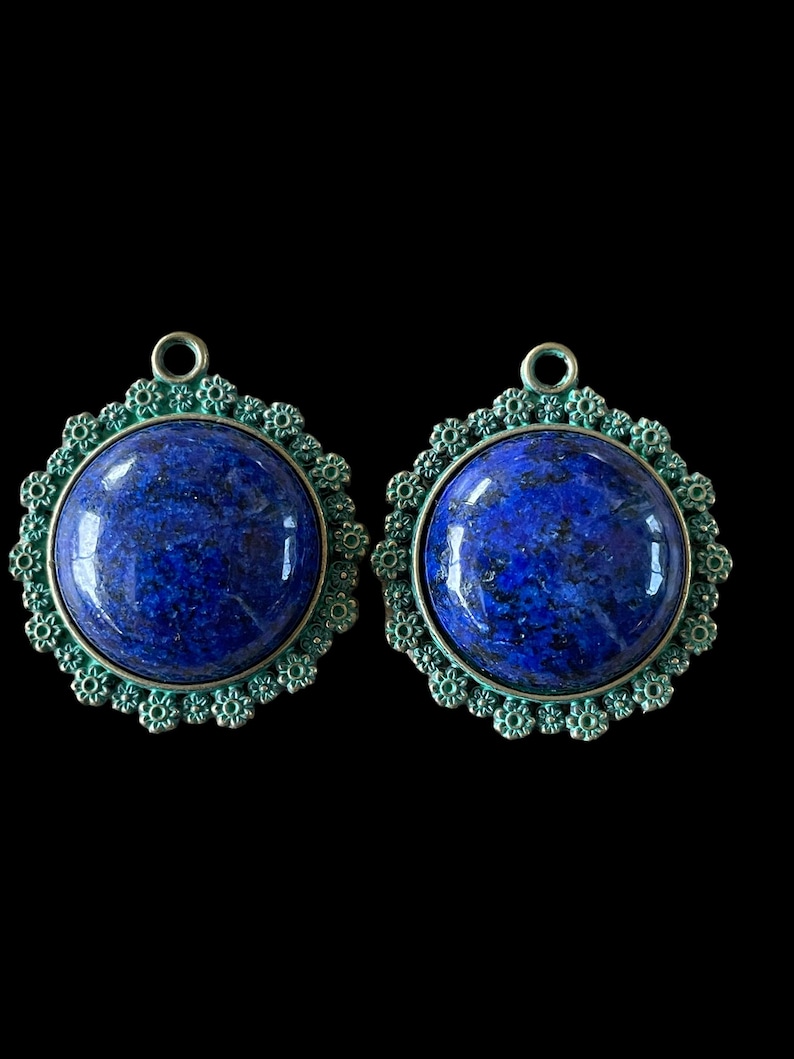 Op de afbeelding: Twee ronde blauwe lapis lazuli edelsteen hangers met een groen filigraan metalen ontwerp.