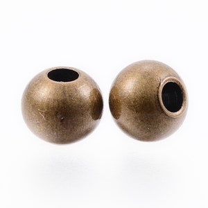 May include: Two antique gold-colored metal beads with a hole in the center. The beads are round and smooth.