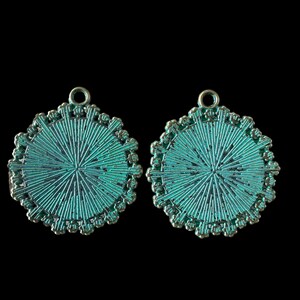 Op de afbeelding: Twee ronde turquoise metalen bedels met een decoratief ontwerp en een lus aan de bovenkant.