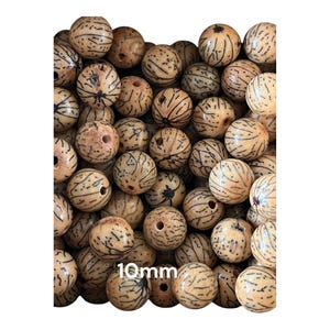Op de afbeelding: Een close-up van een stapel van 10 mm natuurlijke bruine zaad kralen met zwarte markeringen. De kralen zijn rond en hebben een gat in het midden.
