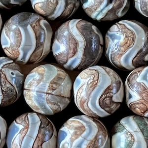 Peut inclure: Un ensemble de perles rondes en agate avec un motif tourbillonnant de brun, blanc et gris. Les perles sont lisses et polies.