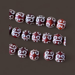 May include: A string of dark red beads with white swirling patterns. The beads are round and have a smooth, polished finish.