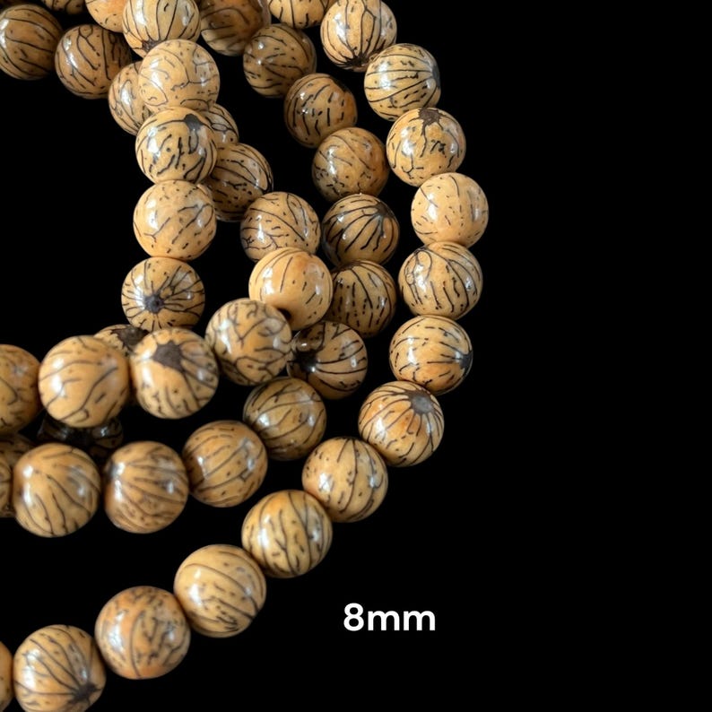Op de afbeelding: Een close-up van een streng natuurlijke houten kralen met een lichtbruine kleur en een donkerbruin patroon. De kralen zijn 8 mm in diameter.