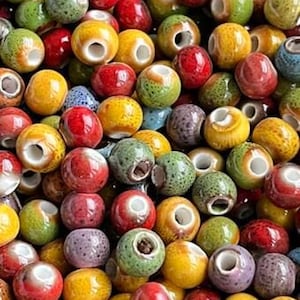 Peut inclure: Un ensemble de perles en céramique colorées avec un trou au centre. Les perles sont de différentes nuances de rouge, vert, jaune et marron.
