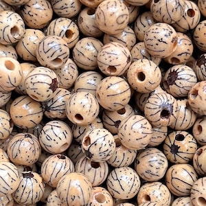 Op de afbeelding: Een close-up van een stapel natuurlijke houten kralen. De kralen zijn rond en hebben een lichtbruine kleur met donkerbruine lijnen die er doorheen lopen. Elke kraal heeft een gat dat door het midden is geboord.