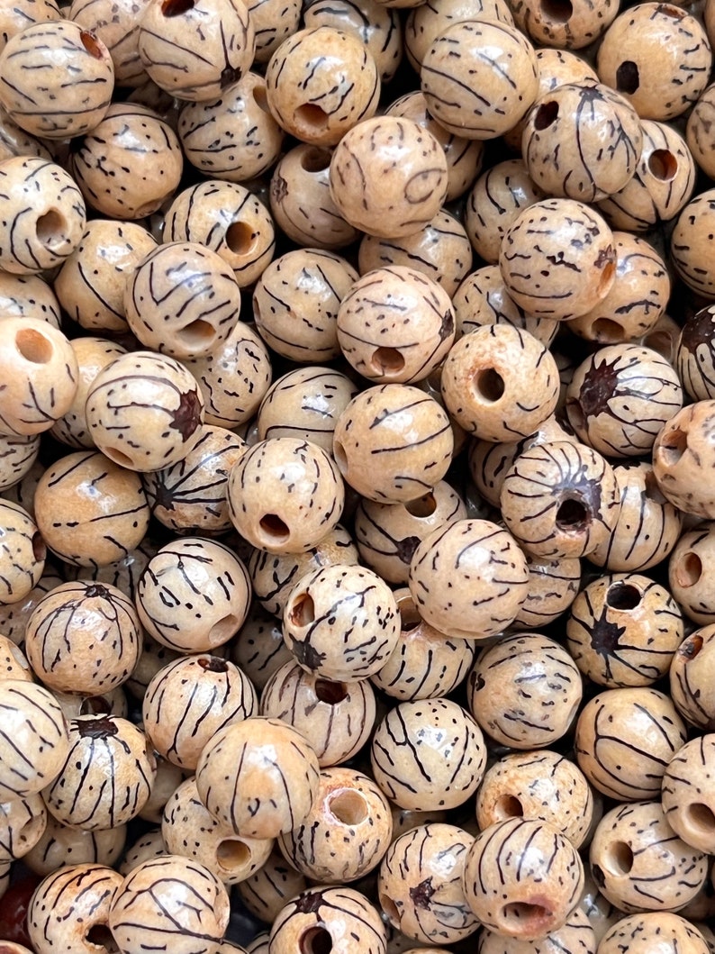 Op de afbeelding: Een close-up van een stapel natuurlijke houten kralen. De kralen zijn rond en hebben een lichtbruine kleur met donkerbruine lijnen die er doorheen lopen. Elke kraal heeft een gat dat door het midden is geboord.