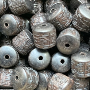 Puede incluir: Primer plano de un montón de cuentas de madera negra con tallas intrincadas. Las cuentas son cilíndricas y tienen un agujero en el centro. Son perfectas para hacer joyas u otras artesanías.