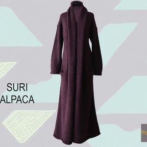 May include: A long, dark purple, open-front coat with long sleeves and a shawl collar. The garment features a textured knit surface and two side pockets. The text "SURI ALPACA" is printed on the left, and "PopsFL" is in the bottom right corner.