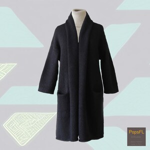 May include: A long, black cardigan with a shawl collar and two pockets. The cardigan is made of a soft, knitted fabric.