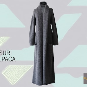 May include: A long, dark gray open-front coat with a wide shawl collar and long sleeves. The text SURI ALPACA is printed on the left side, and the text PopsFL is printed in a small gray square in the bottom right corner of the image.