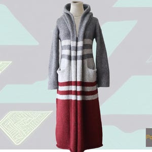 Könnte beinhalten: Ein langer, grau-roter gestreifter Cardigan mit Kapuze und Taschen. Der Cardigan ist aus weichem, gestricktem Stoff.